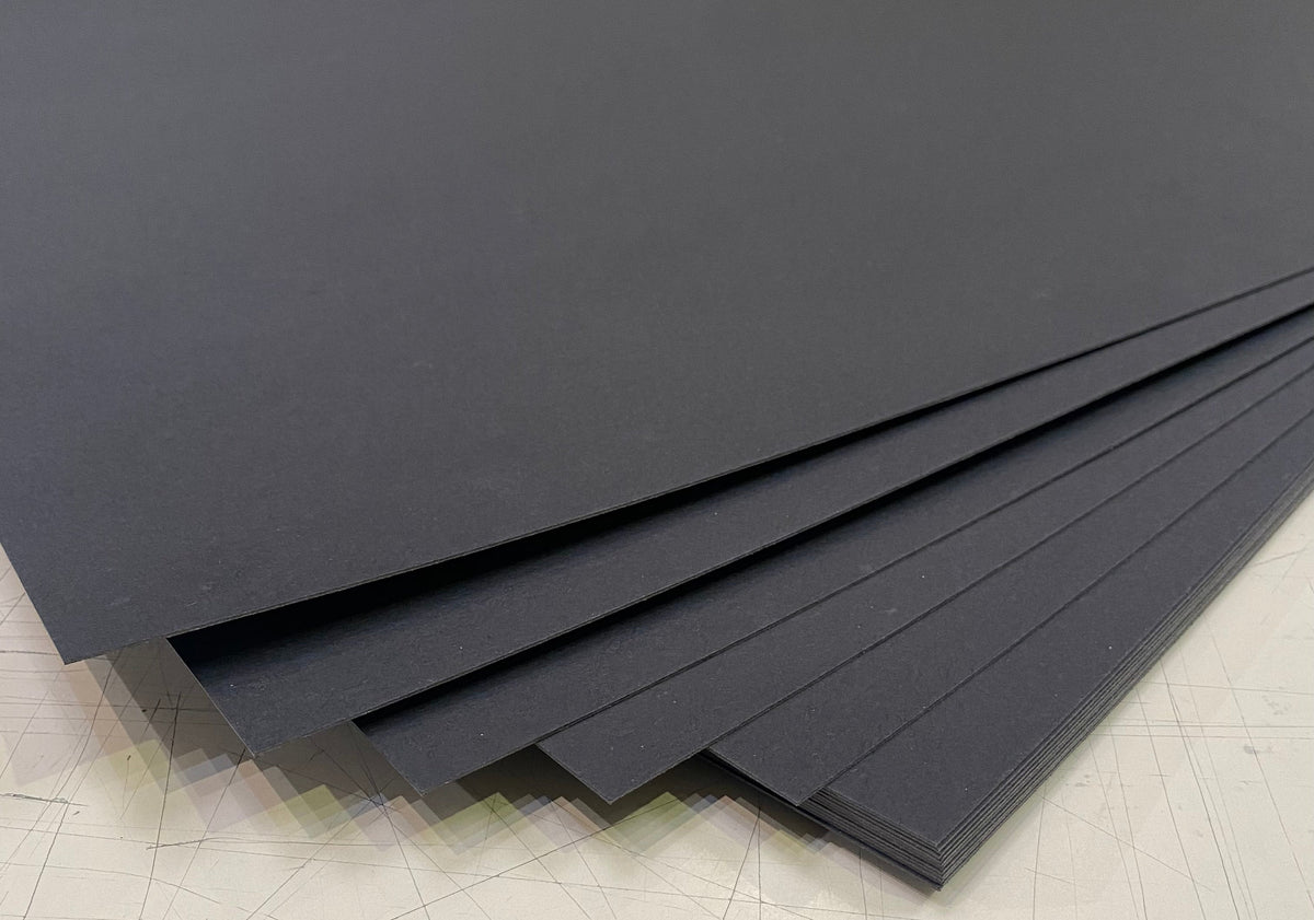 A stack of matte black rectangular sheets or panels fanned out on a light gray scratched surface.