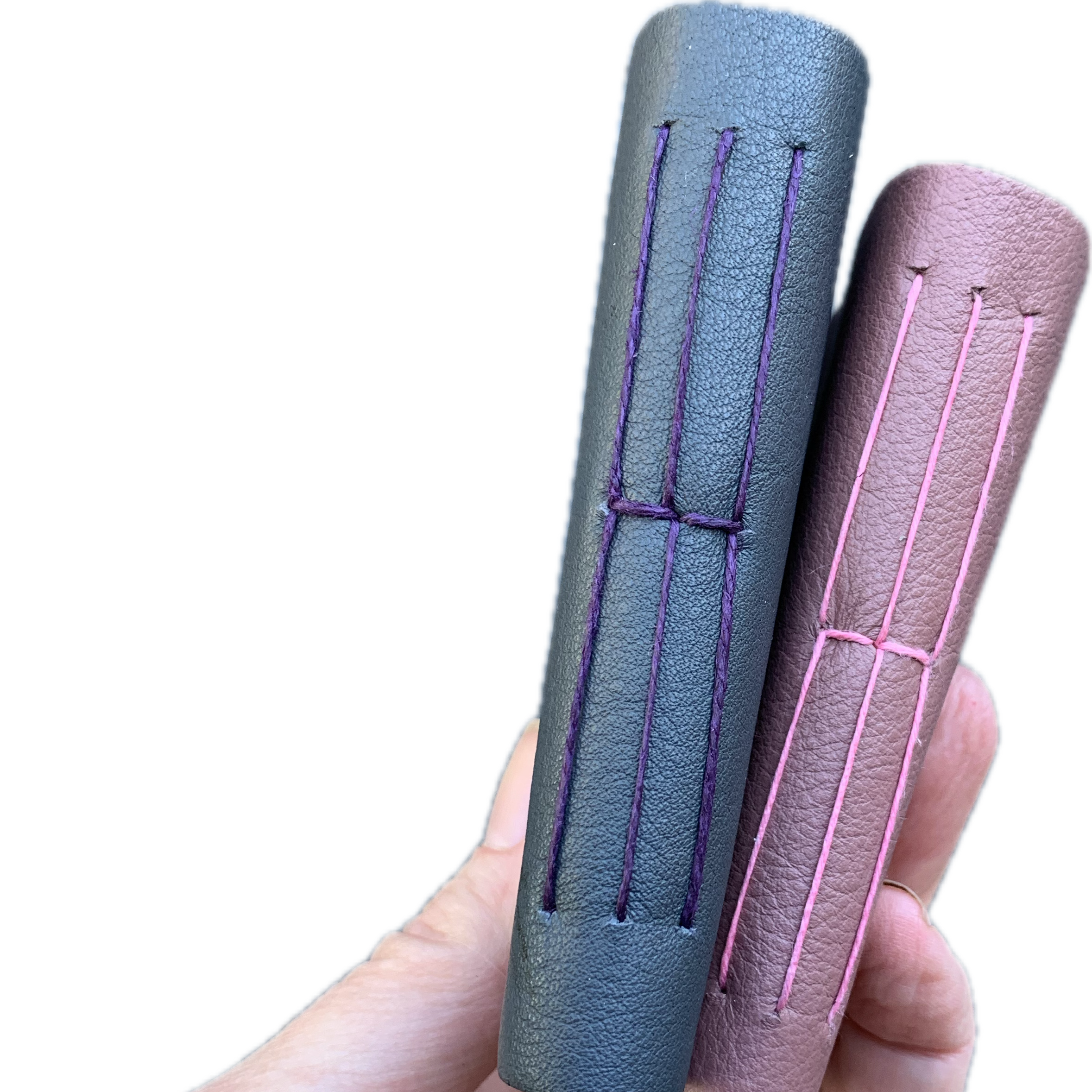 A hand holding two leather-wrapped journals in purple and gray colors.