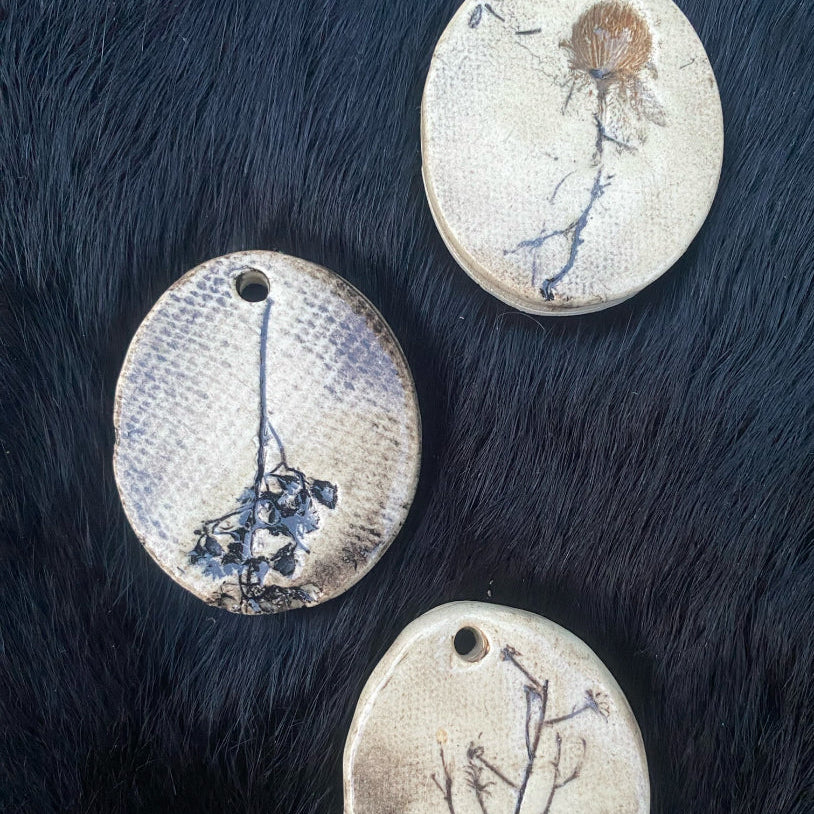 Three round ceramic pendants with floral designs on a dark fur background