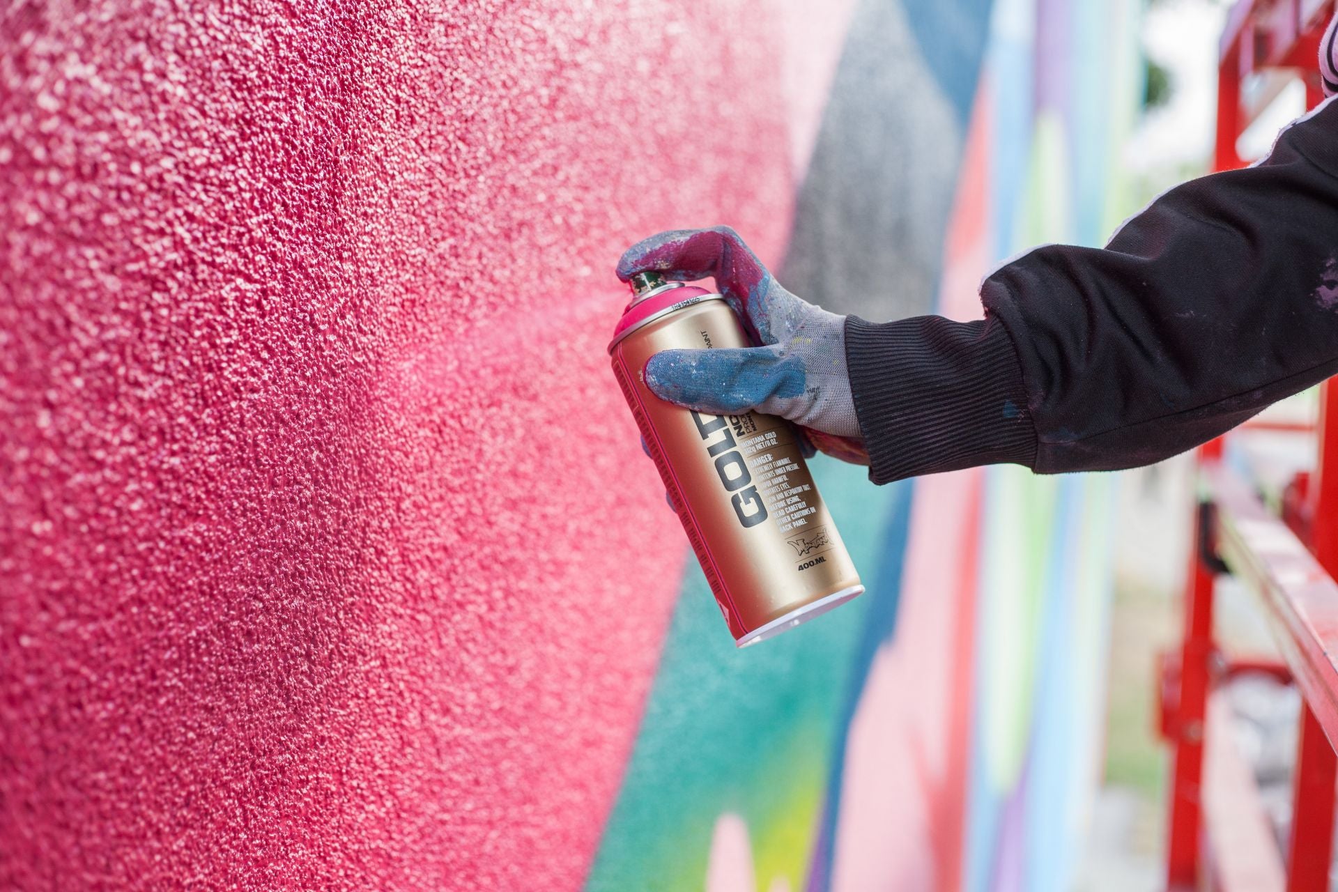 Person holding a spray can against a colorful graffiti wall
