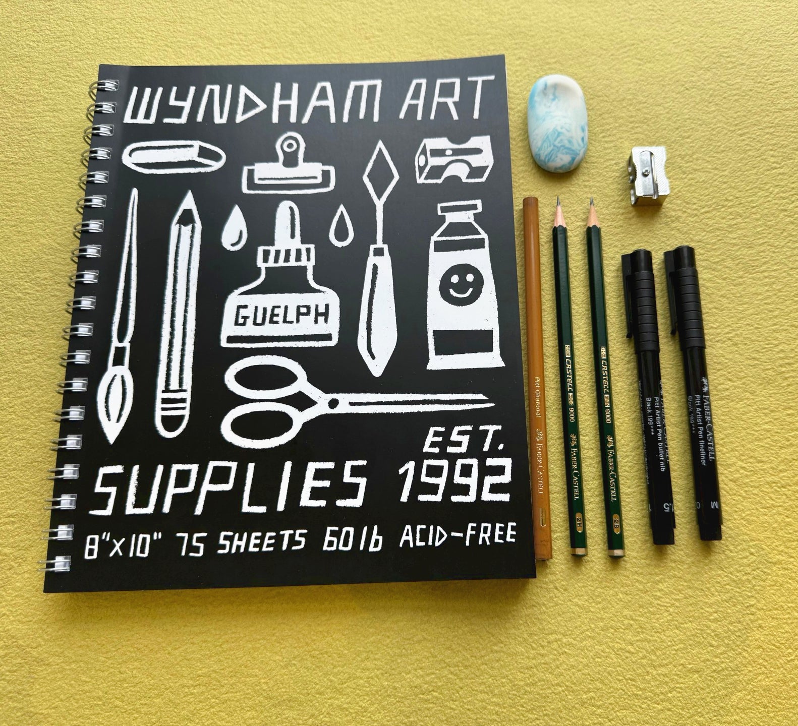 Wyndham Art Supplies notebook with stationery items on a yellow background